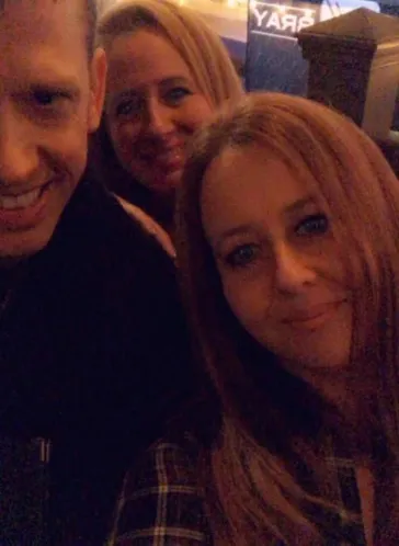 Three fans smiling together at a show near the Mark Bray backdrop