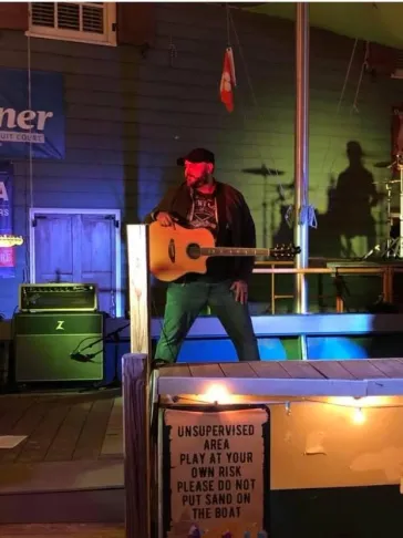 Mark performing acoustic guitar on an outdoor dock stage at night