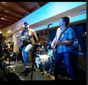 Full band performing on stage with blue lighting and drum kit visible