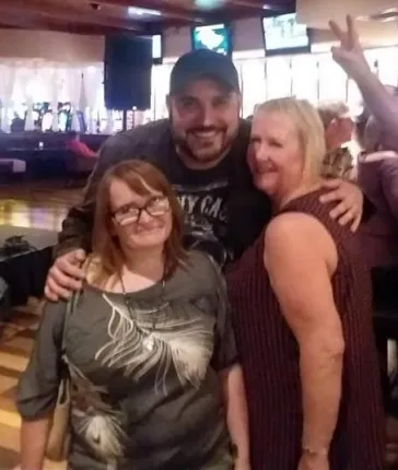 Mark posing with two fans at a bar table
