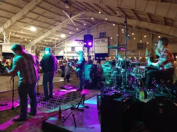 Full band performing under purple and cyan stage lighting in a large venue