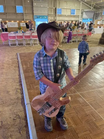 Young fan in a cowboy hat holding a guitar at an indoor event