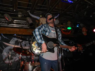Mark performing with acoustic guitar on stage at an indoor venue