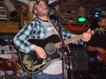 Mark performing with acoustic guitar and smiling on stage