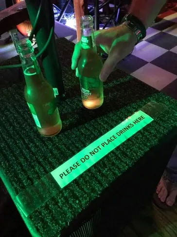 Bud Light bottles on an amp with a do not place drinks sign under green neon light