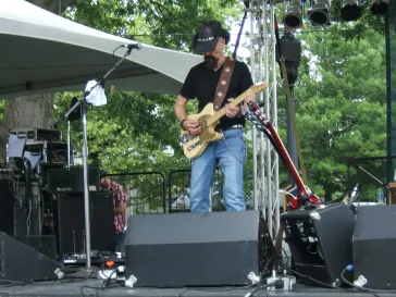 Guitarist performing on an outdoor stage under a white tent