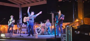 Full band performing with arms raised on stage