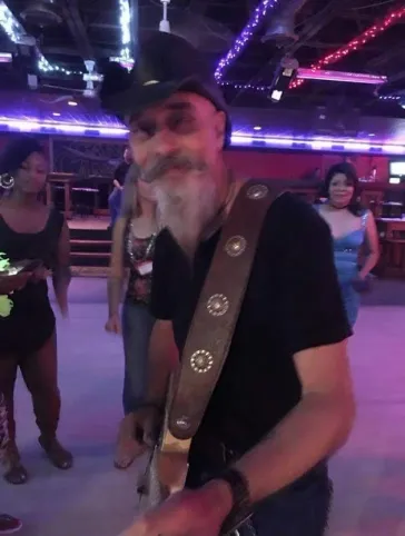 Dino with guitar strap at a neon-lit country bar